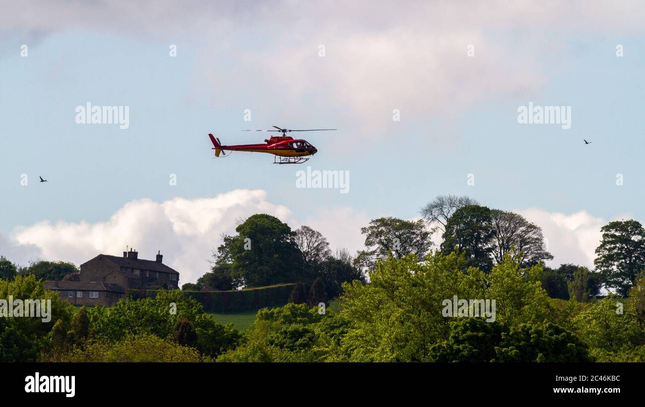 Red and Yellow Helicopter G ORKY fliegen tief in der Nähe von Häusern, Burley-in-Wharfedale, Großbritannien Stockfoto