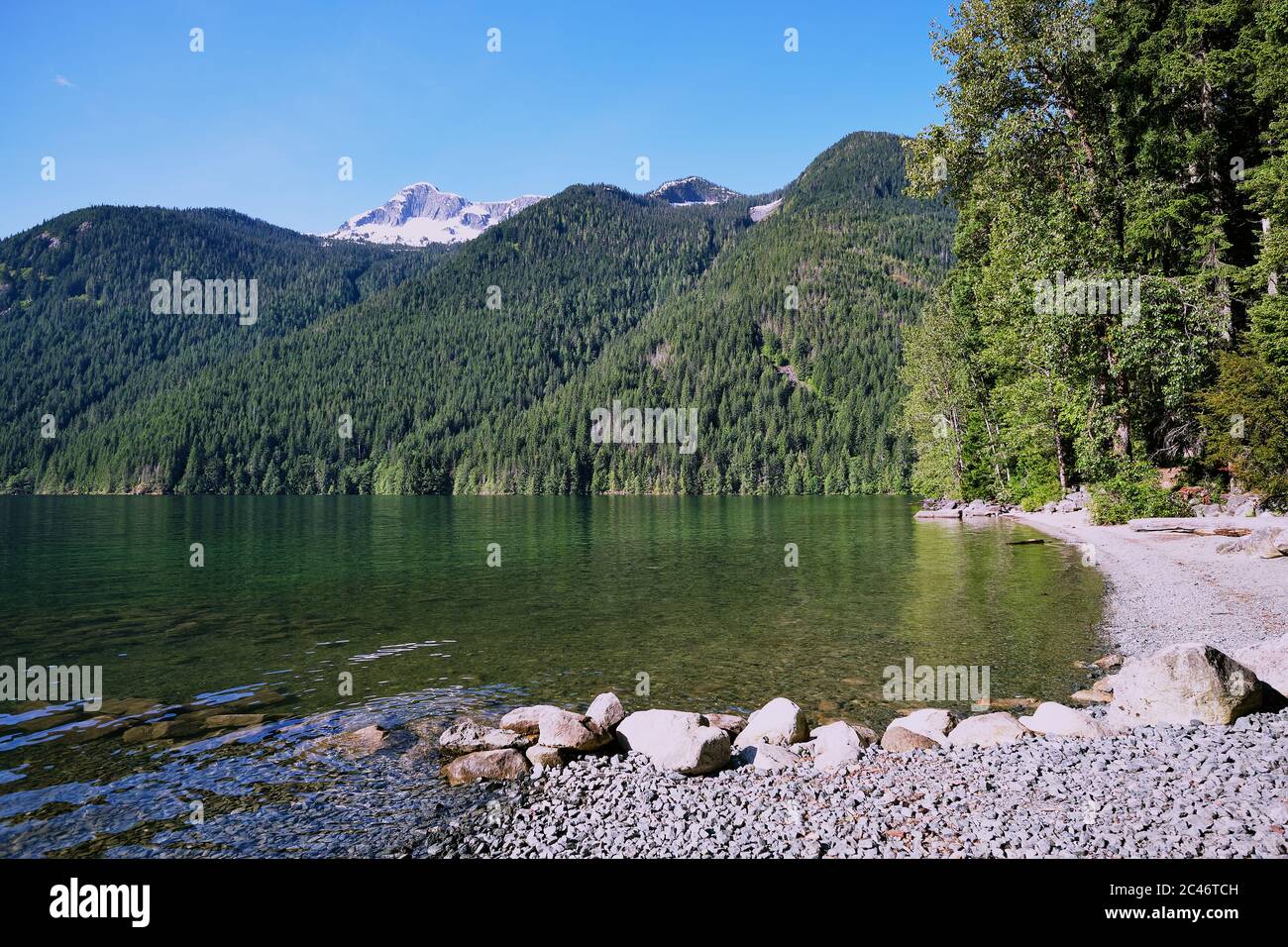 Strand und Bootsanlegestelle am Chilliwack Lake (Sxotsaquel), BC. Hoch über Hängen mit Nadelbäumen bewaldet sind hohe Berge mit freiliegenden Felswänden und Stockfoto