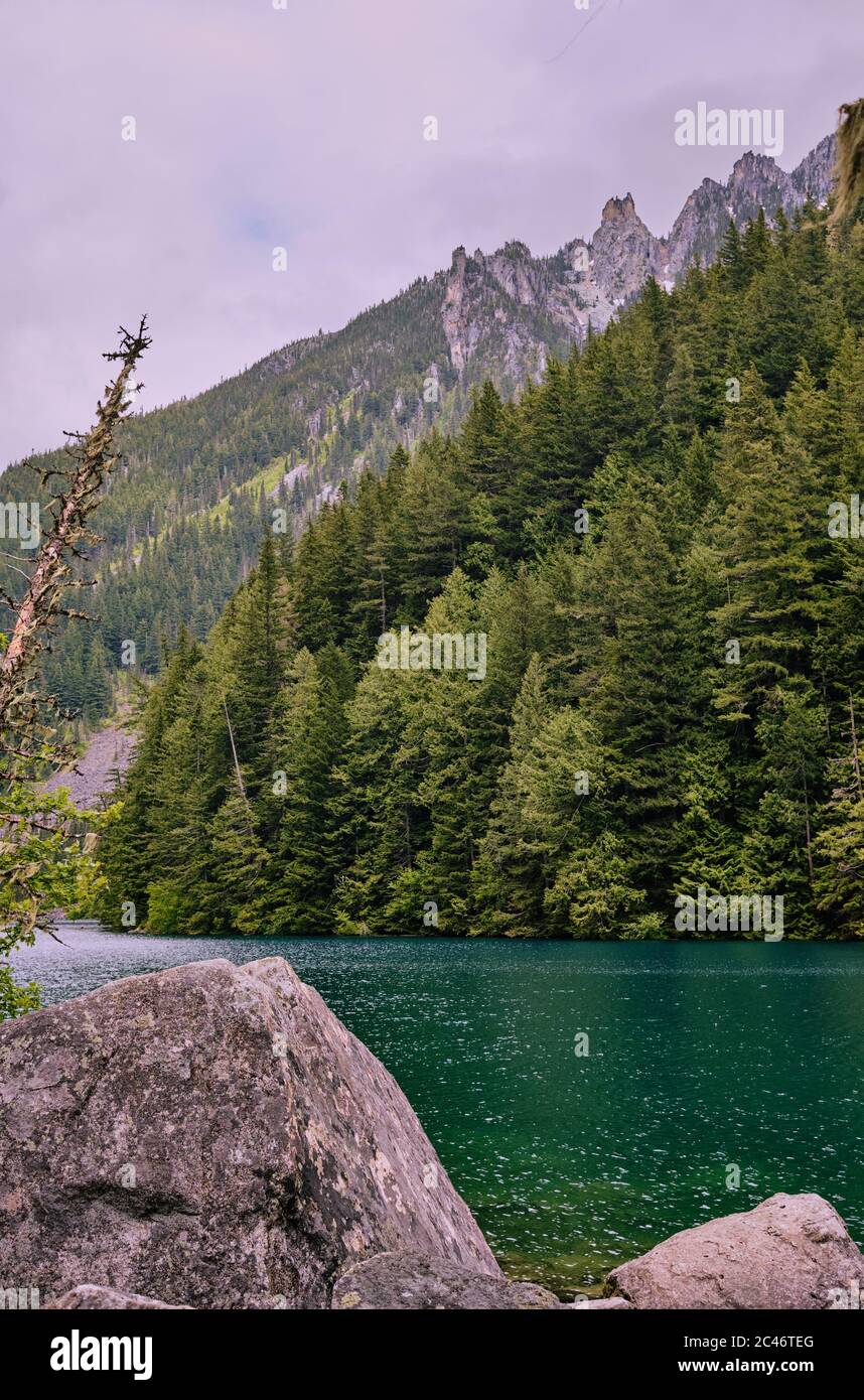 Smaragdgrünes Wasser des Lindeman Lake in Chilliwack, Provincial Park Ruhe unter steilen bewaldeten Hängen, Felsbrocken und schroffen Berggipfeln Stockfoto