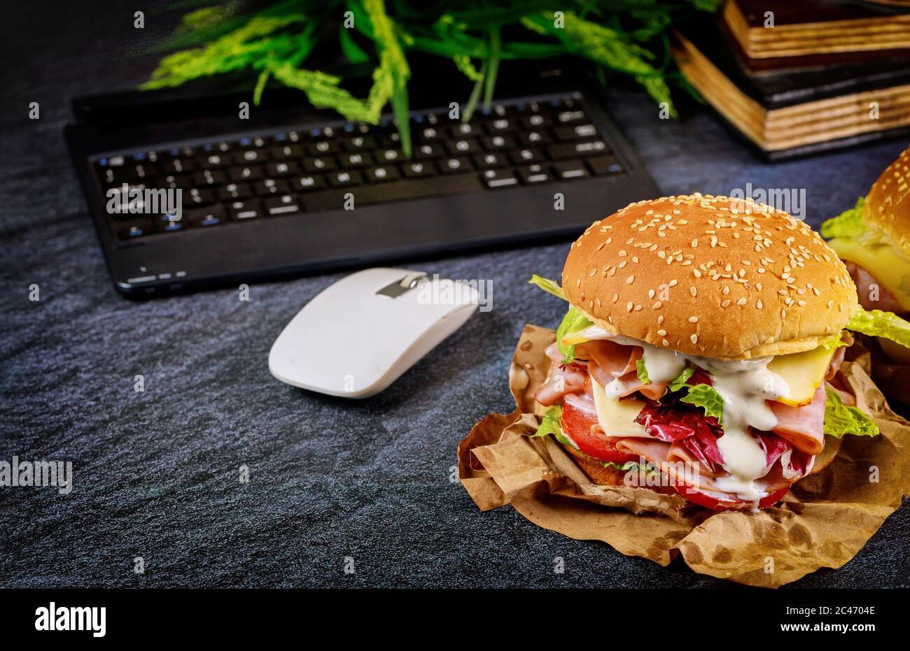 Sandwich auf dunklem Schreibtisch mit Tastatur, Maus und Büchern. Arbeiten Sie von zu Hause aus. Stockfoto