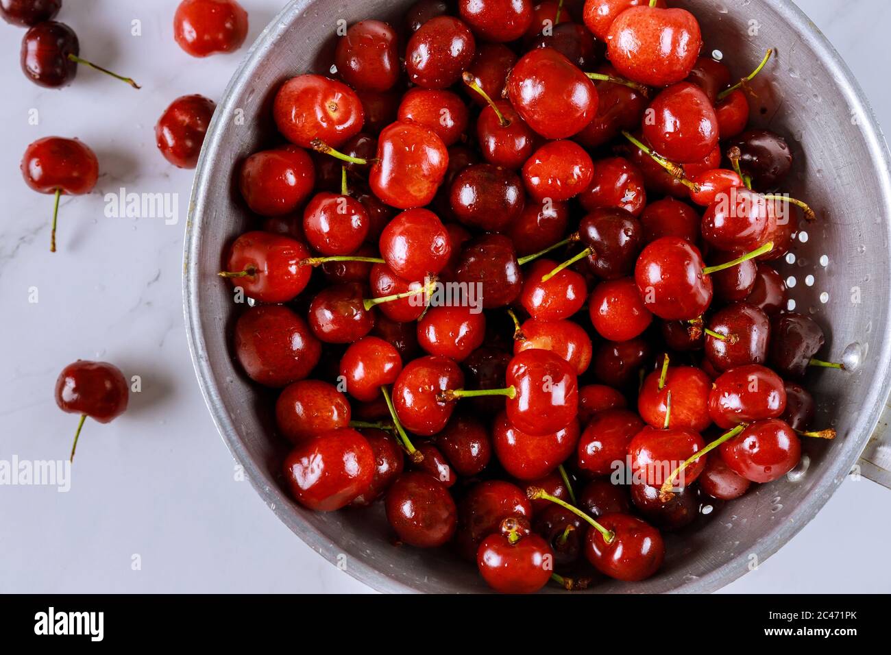 Frische Süßkirschen in einer Sieb-Schüssel mit Wassertropfen auf weißem Hintergrund. Draufsicht. Stockfoto
