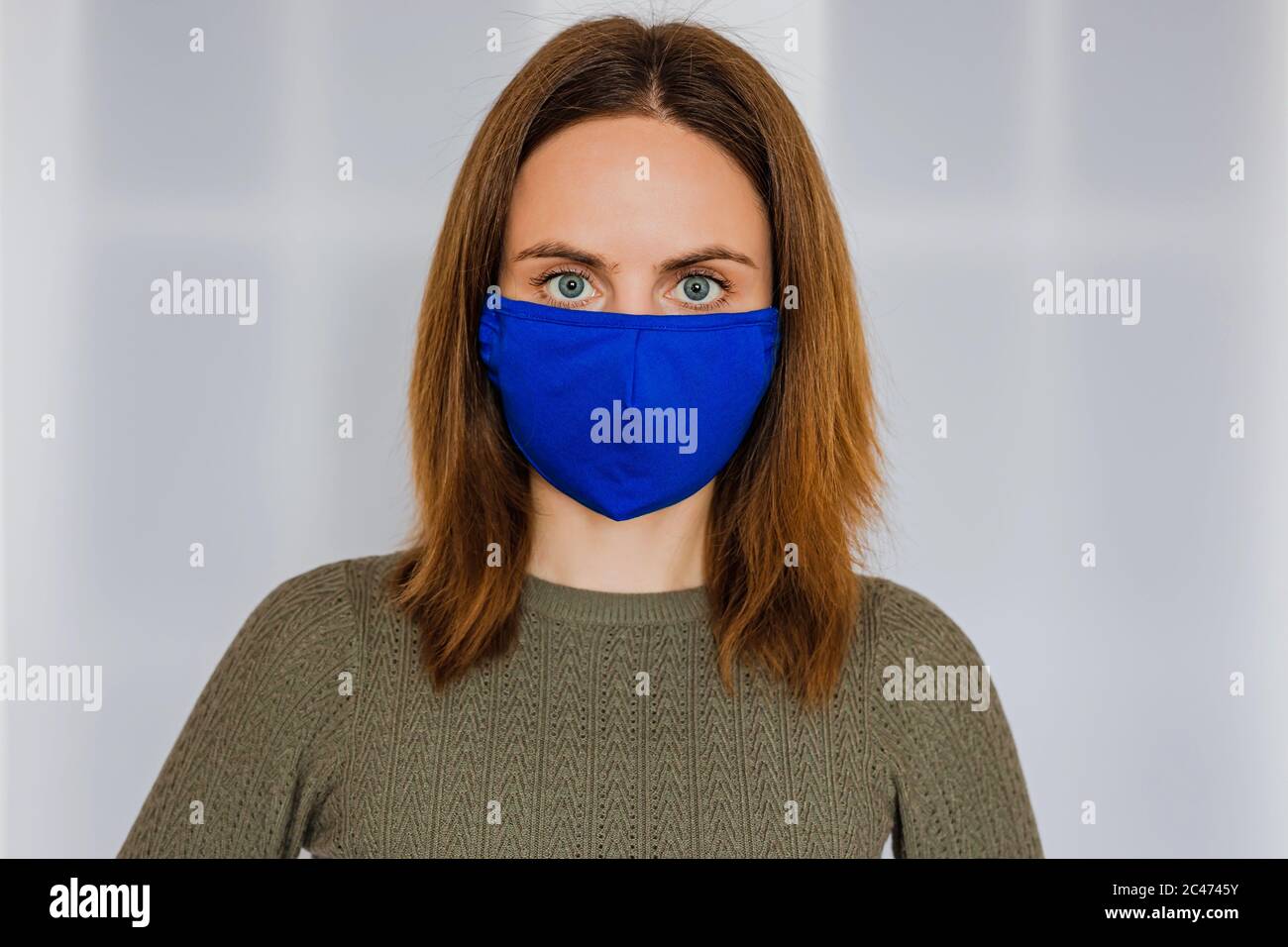 Eine junge kaukasische Frau mit hellbraunen Haaren in einer blauen medizinischen Gesichtsmaske Stockfoto