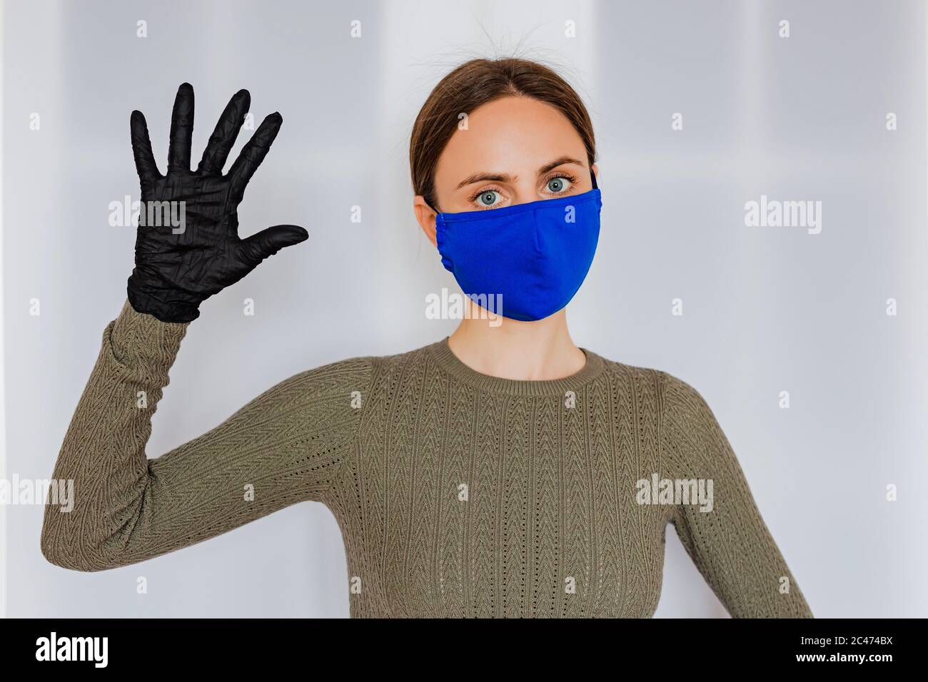 Eine junge kaukasische Frau mit hellbraunen Haaren in einer blauen medizinischen Gesichtsmaske aus Baumwolle und schwarzen medizinischen Latexhandschuhen Stockfoto