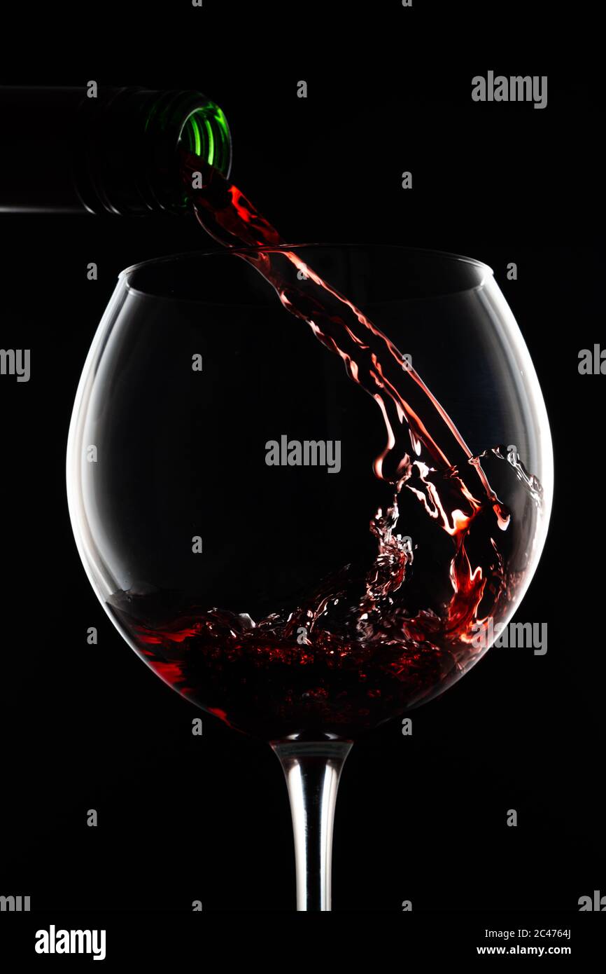 Glas Rotwein und Flasche auf schwarzem Hintergrund Stockfoto