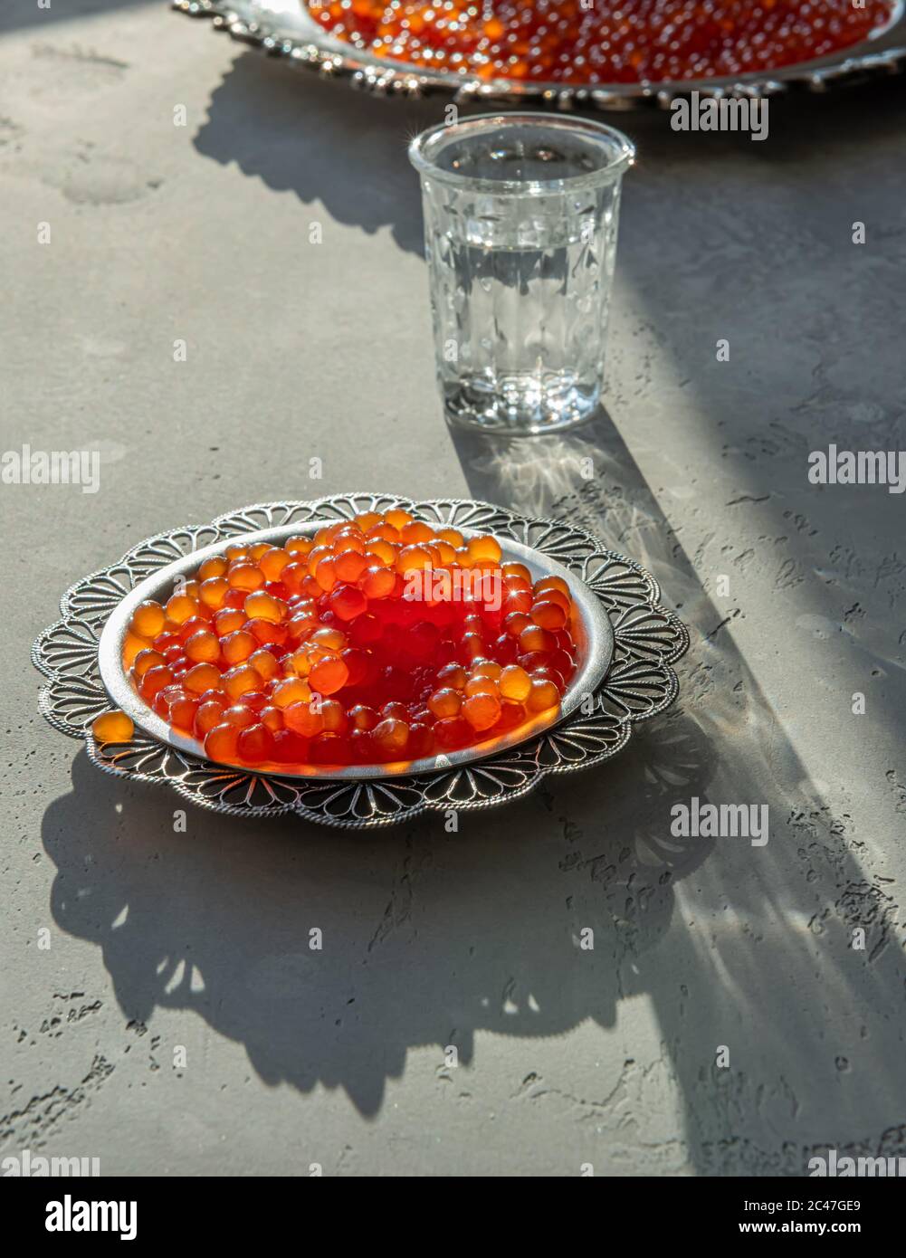 Natürlicher roter Kaviar auf silbernem Teller auf grauem Hintergrund. Wodka Schüsse und Teller mit Kaviar auf unfokussierten Hintergrund. Selektiver Fokus. Gesunde Ernährung concep Stockfoto