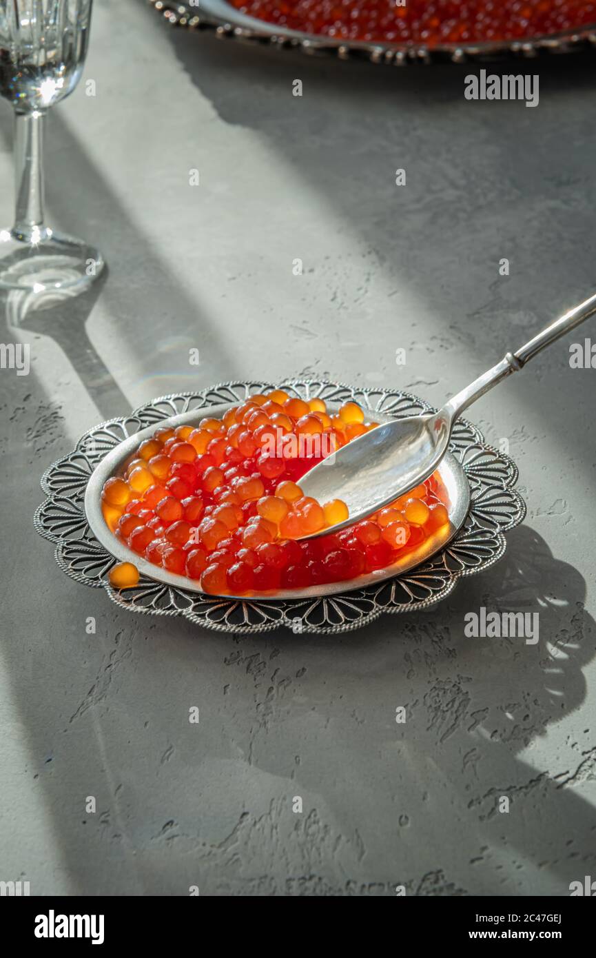 Natürlicher roter Kaviar auf silbernem Teller auf grauem Hintergrund. Wodka Schüsse und Teller mit Kaviar auf unfokussierten Hintergrund. Selektiver Fokus. Gesunde Ernährung concep Stockfoto