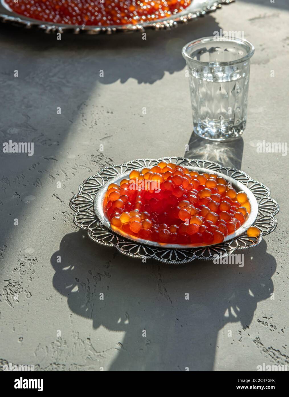 Natürlicher roter Kaviar auf silbernem Teller auf grauem Hintergrund. Wodka Schüsse und Teller mit Kaviar auf unfokussierten Hintergrund. Selektiver Fokus. Gesunde Ernährung concep Stockfoto