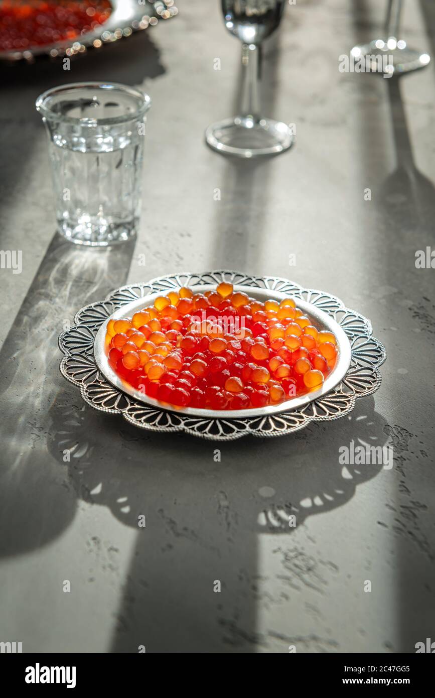 Natürlicher roter Kaviar auf silbernem Teller auf grauem Hintergrund. Wodka Schüsse und Teller mit Kaviar auf unfokussierten Hintergrund. Selektiver Fokus. Gesunde Ernährung concep Stockfoto