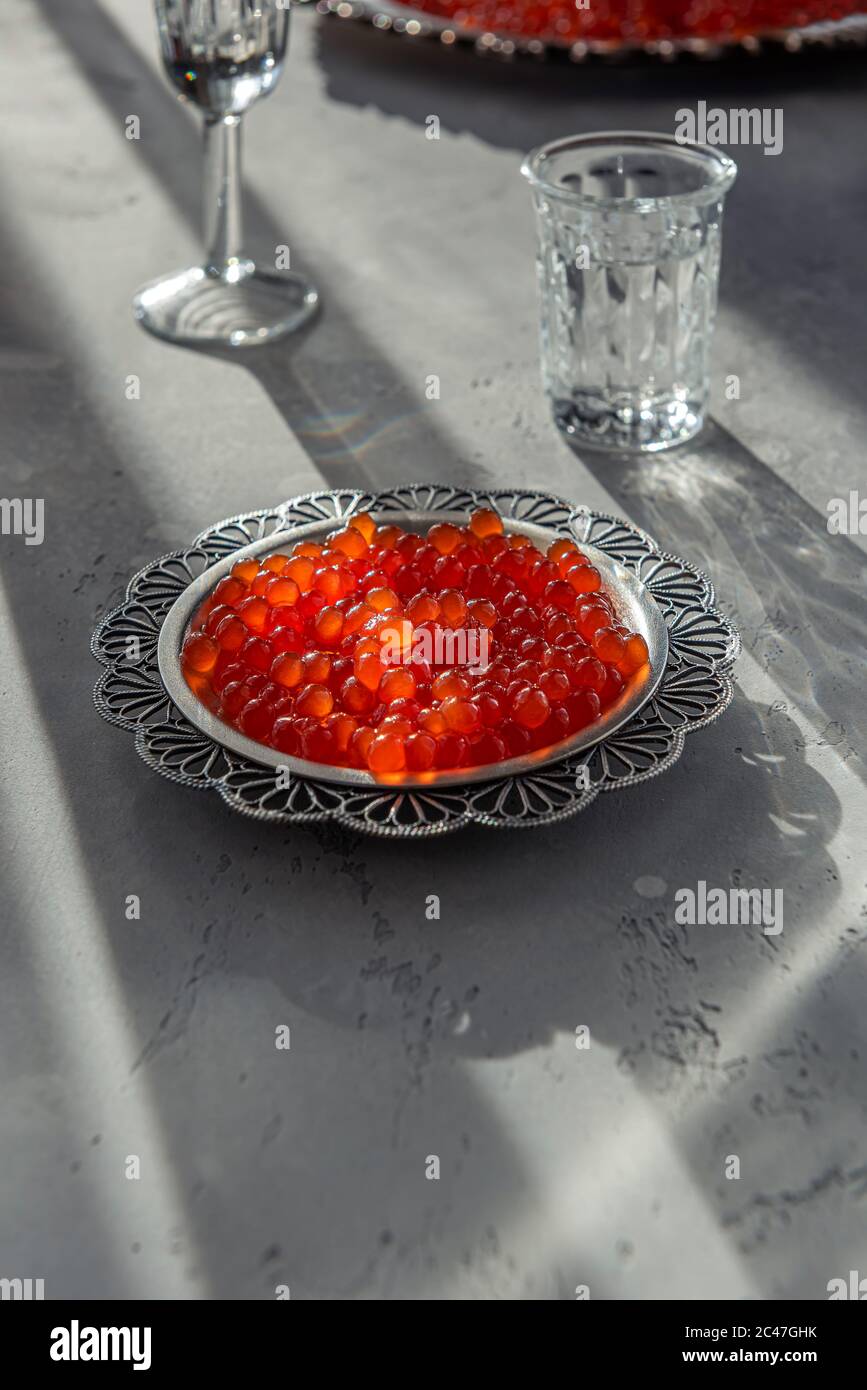 Natürlicher roter Kaviar auf silbernem Teller auf grauem Hintergrund. Wodka Schüsse und Teller mit Kaviar auf unfokussierten Hintergrund. Selektiver Fokus. Gesunde Ernährung concep Stockfoto