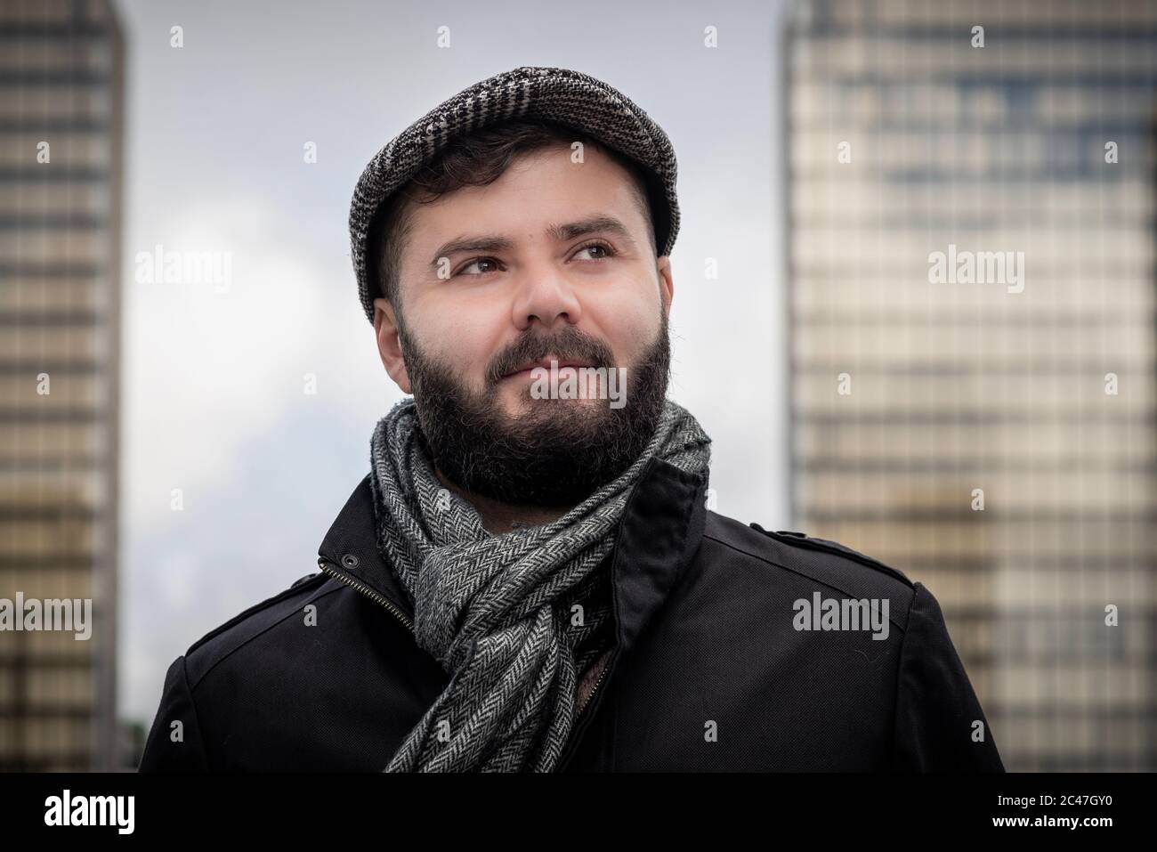 Junger hübscher französischer bärtiger Mann, draußen mit Gebäuden hinter dem Hotel mit natürlichem Licht in Paris, Frankreich, aufgenommen Stockfoto