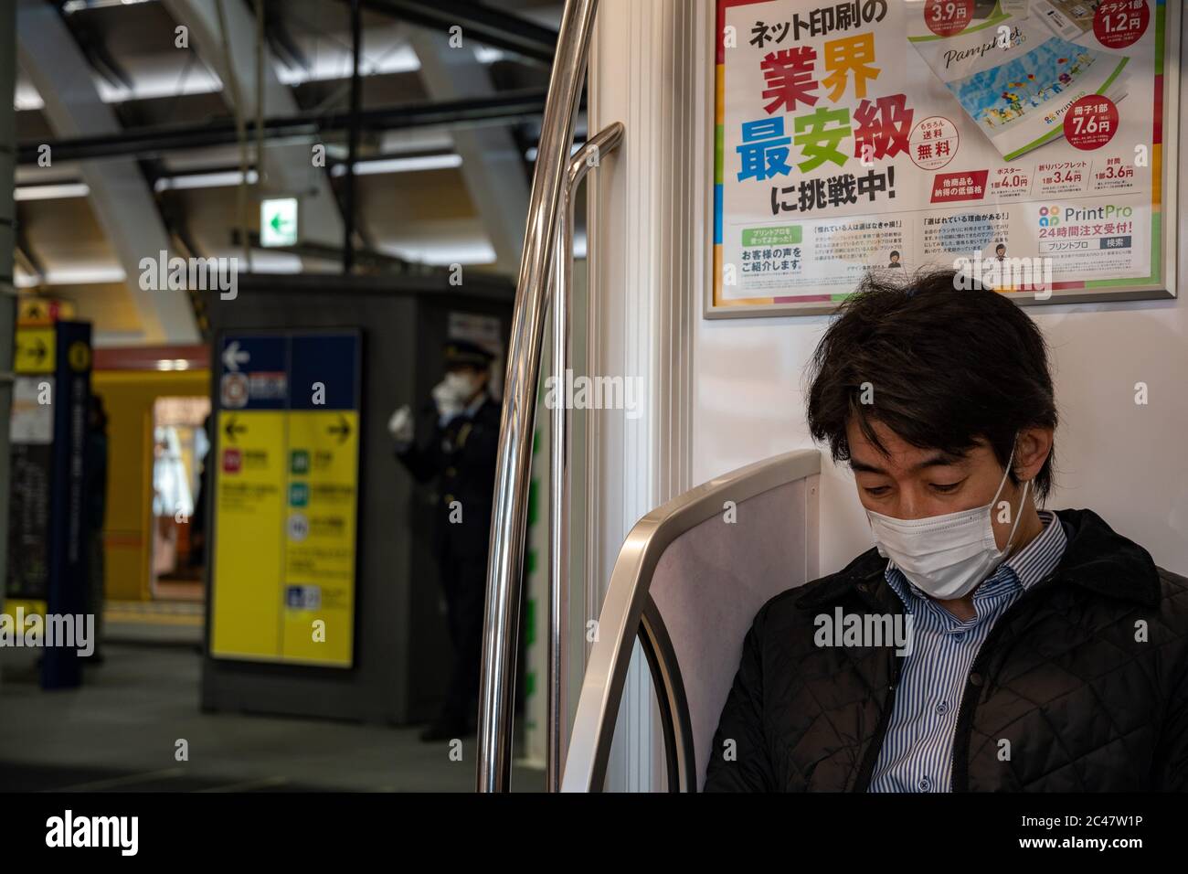 Ein junger Mann mit Gesichtsmaske sitzt auf einem Ginza-Linienwagen. Im Hintergrund hielt die U-Bahn-Station mit einem gelben Fahrzeug auf der gegenüberliegenden Gleise. Stockfoto