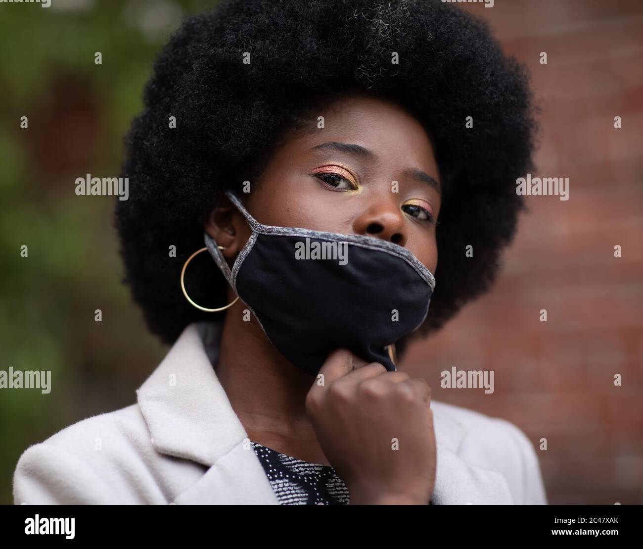 Schwarze selbstbewusste Frau, die ihre Gesichtsmaske herunterzieht. Gesichtsbedeckung ist während der COVID-19-Pandemie obligatorisch in der Öffentlichkeit zu tragen. Stockfoto