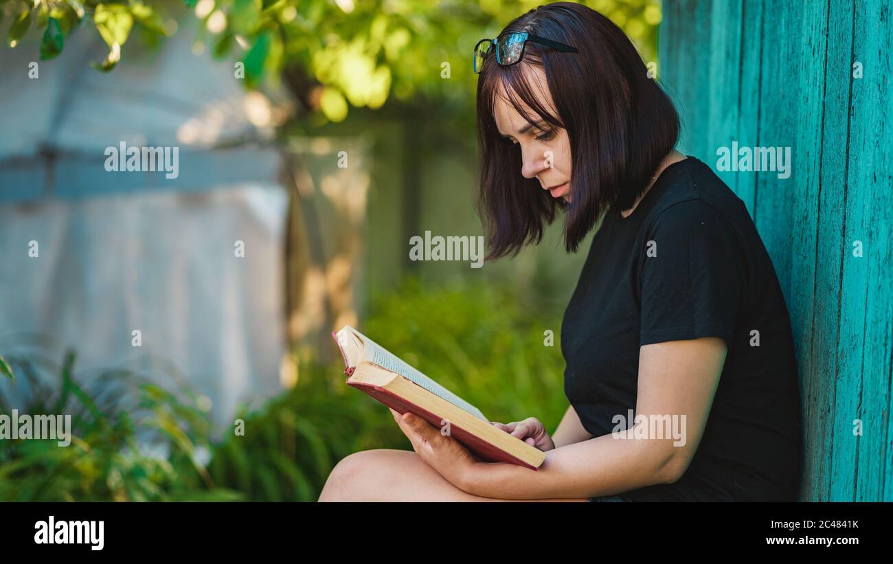 Nahaufnahme einer jungen Frau, die im Garten ein Buch liest. Weibliche Ruhe in der Natur, genießen ihre Freizeit. Stockfoto