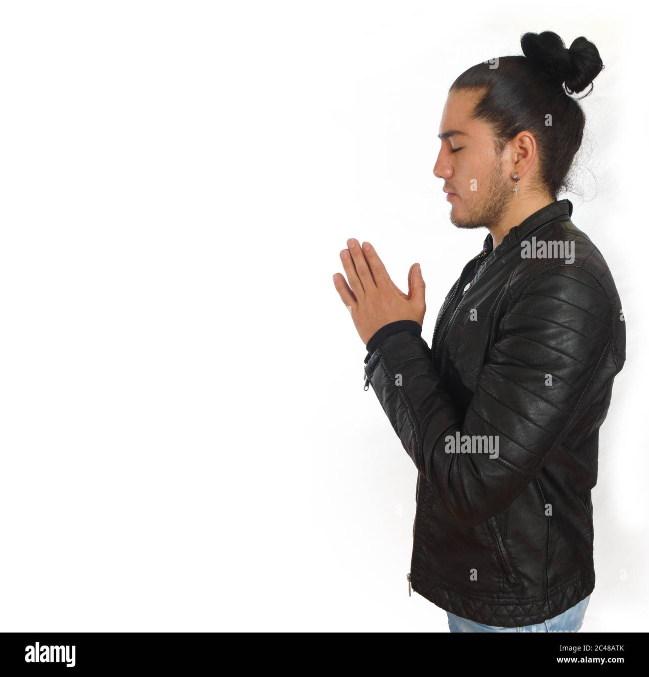 Junger hispanischer Mann mit gerafftem Haar fertig Bogen in schwarzem Hemd und schwarzer Lederjacke gekleidet, mit seinen Händen in Gebetsstellung geklammt, in Pro gesehen Stockfoto