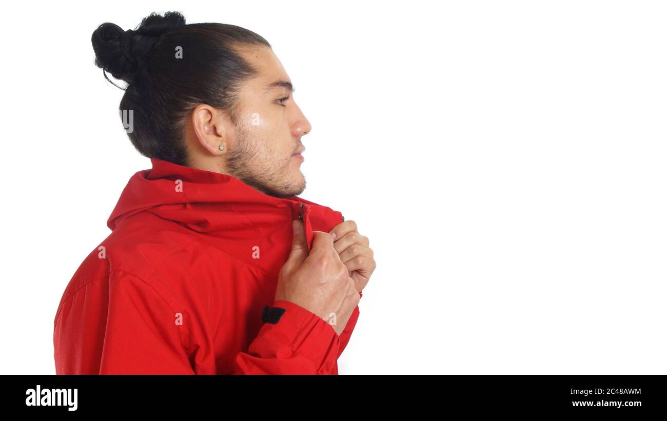 Junger hispanic Mann mit gerafften Haaren getan Bogen trägt schwarzes T-Shirt und rote Jacke, Hände Stretching seine Jacke, posiert Profil nach rechts Stockfoto