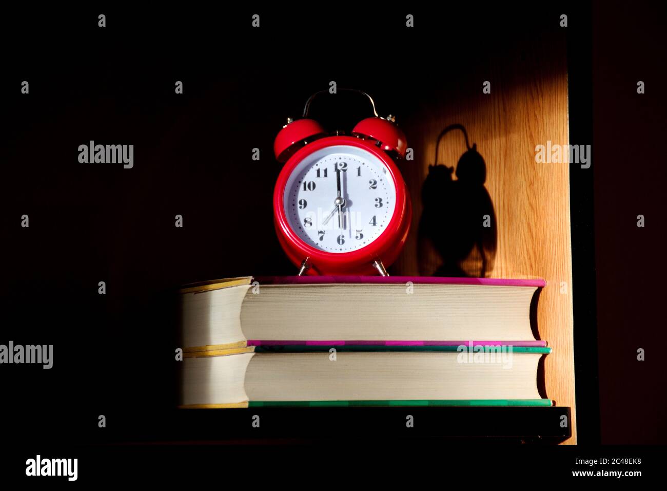 Nahaufnahme der roten Uhr auf den Büchern, die von der aufgehenden Sonne beleuchtet sind Stockfoto