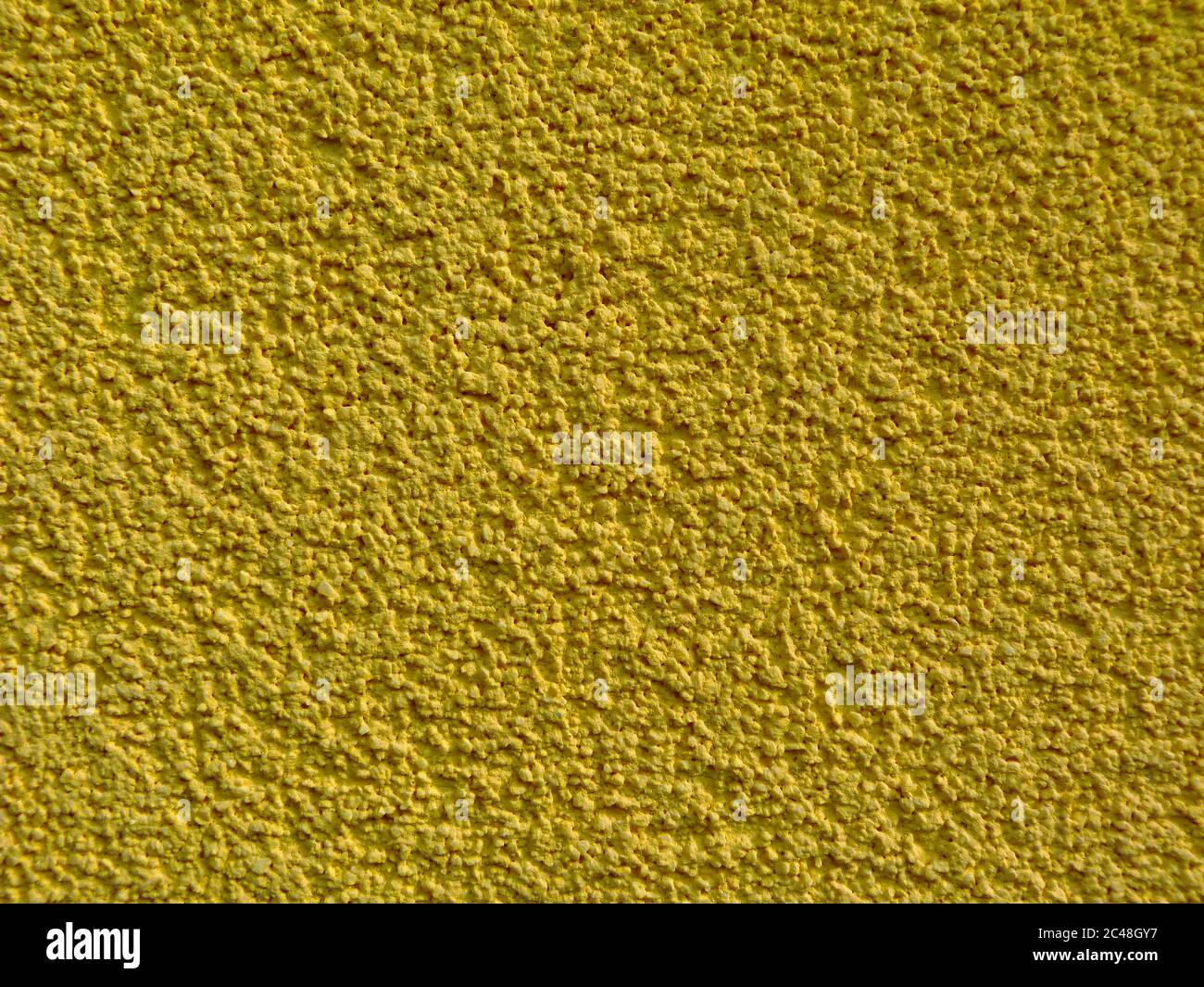Gelbe ockerfarbene Stuckstruktur an der Außenwand mit feinen Körnern. Sandpapier wie sandige, grobkörnige Oberfläche. Nahaufnahme. Muster und Texturen Konzept Stockfoto