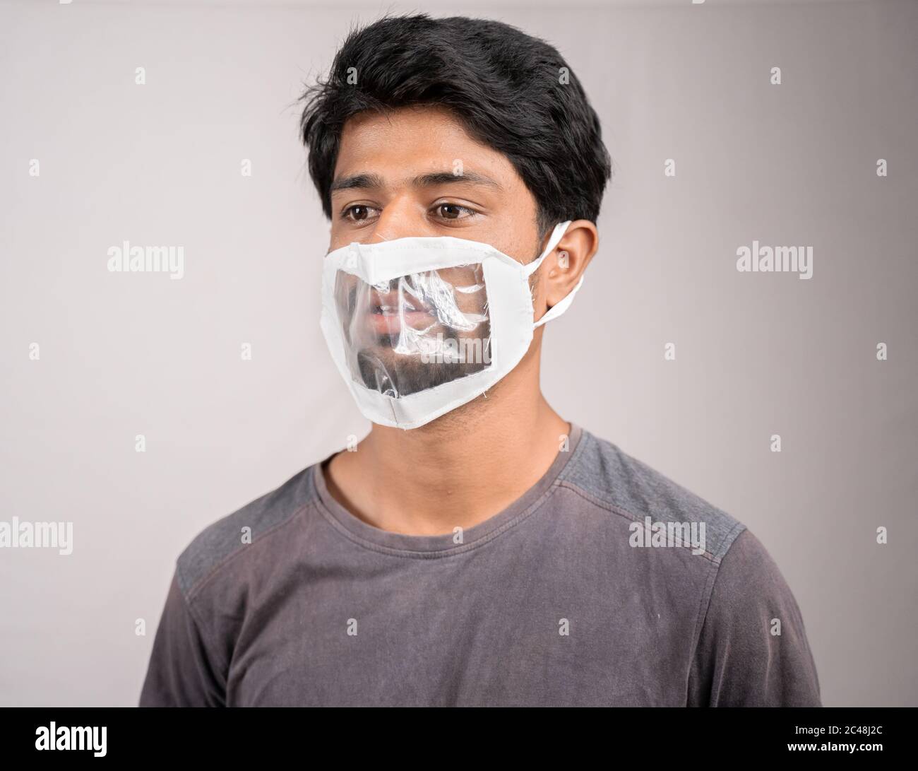Junger Mann mit transparenter medizinischer Gesichtsmaske, um ungezähnt oder taub hörenden Menschen zu helfen, Lipardering während Coronavirus oder covid-19 zu verstehen Stockfoto