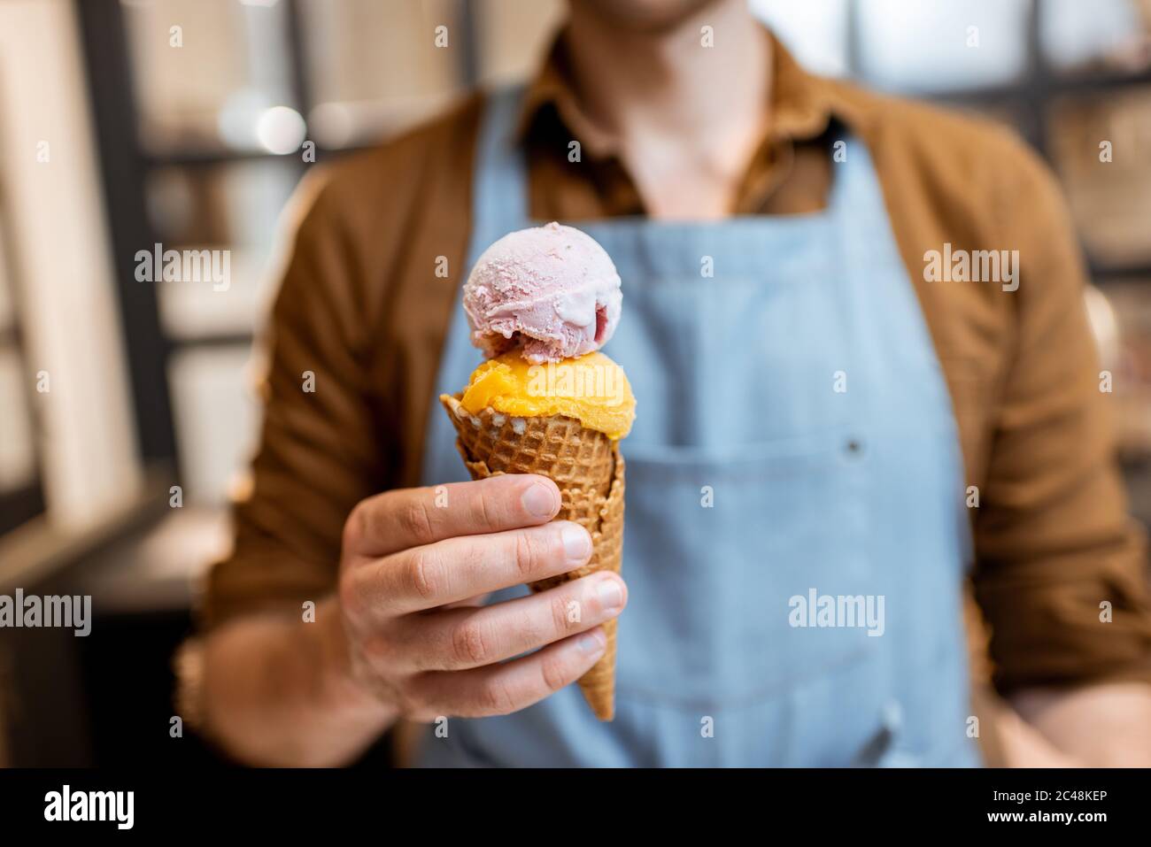 Verkäufer in Schürze hält Eis in einem Waffelkegel, Nahaufnahme. Verkauf von Eis in einem Geschäft Stockfoto