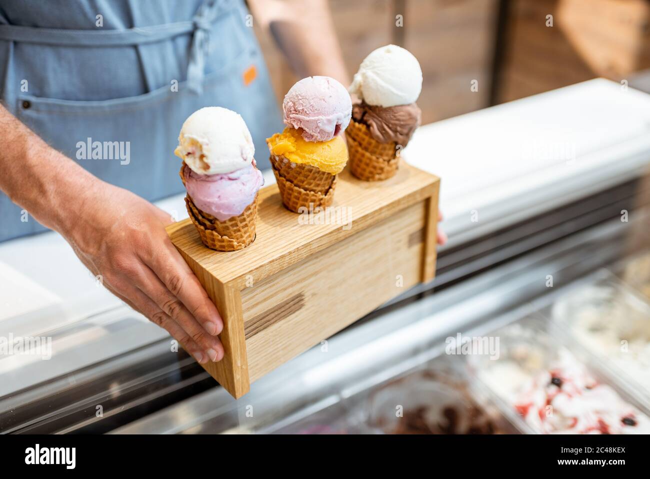 Verkäufer setzt einen Stand mit drei leckeren Eis in Waffelkegel mit verschiedenen Geschmack auf der Theke eines Geschäfts, close-up Stockfoto