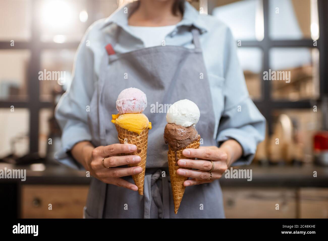 Verkäuferin hält zwei leckere Eiscreme im Waffelkegel im Laden, Nahaufnahme Stockfoto