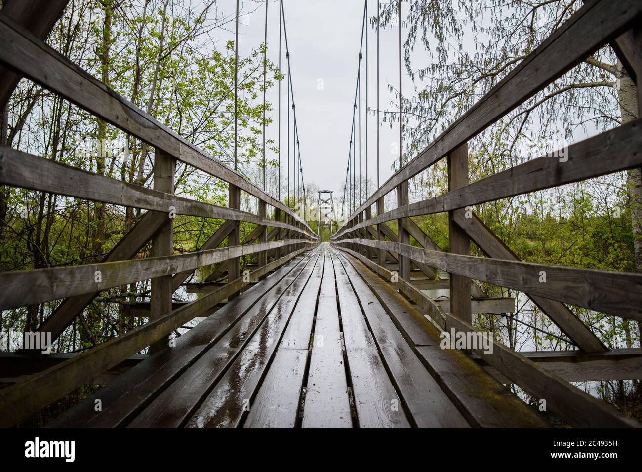 Hölzerne Hängebrücke über den Fluss irgendwo in den Tiefen von Finnland, düsteren bewölkten Tag. Stockfoto