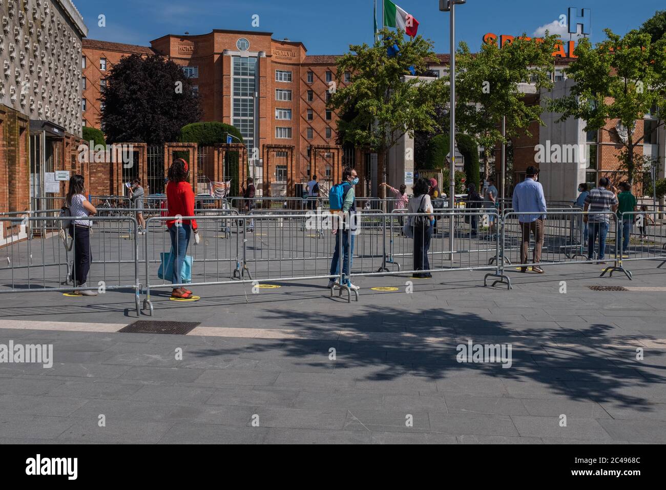 Menschen üben soziale Distanzierung, während sie sich anstellen, um das Zivilkrankenhaus von Brescia während der Coronavirus-Sperre des Landes zu betreten. Gelber Fußboden markiert ihn Stockfoto