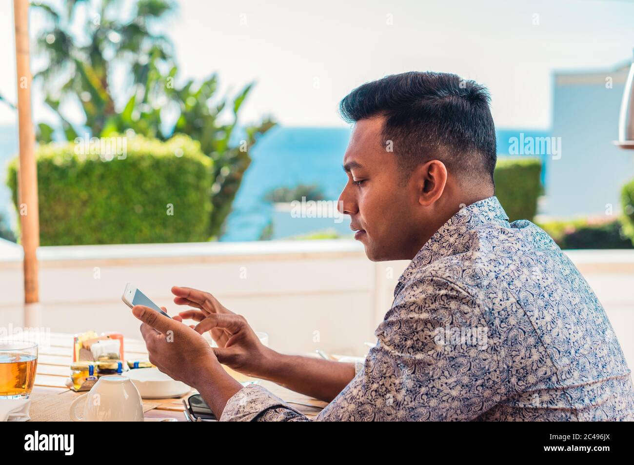 Junger, hübscher Inder, der im Resort mit dem Smartphone im Café sitzt Stockfoto