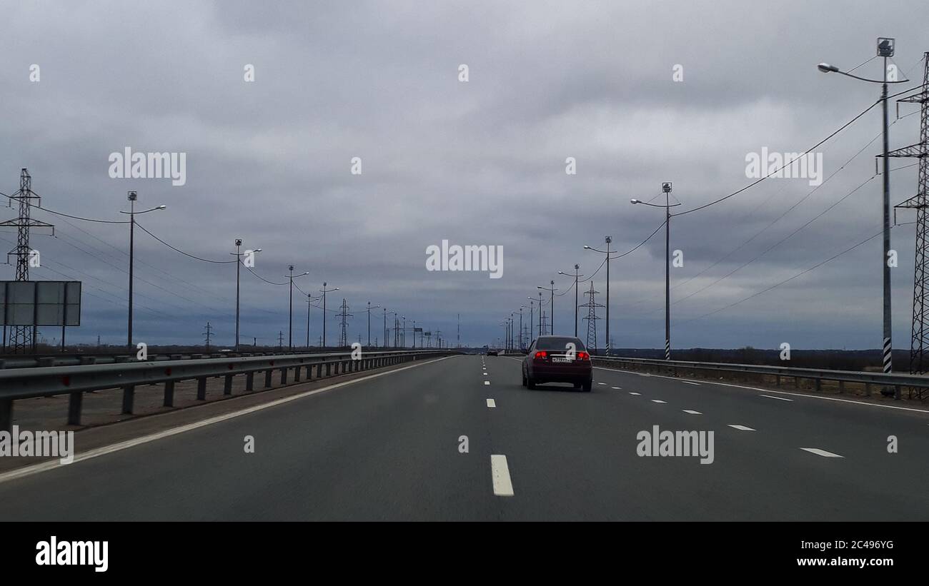 Eine Straße oder eine Autobahn, die Autobahn erstreckt sich bis zum Horizont. Blick vom Fenster des Autos. Reise, der Weg nach Hause. Kalte nördliche Natur, Sommer, grau bewölkt niedrigen Himmel. Stockfoto