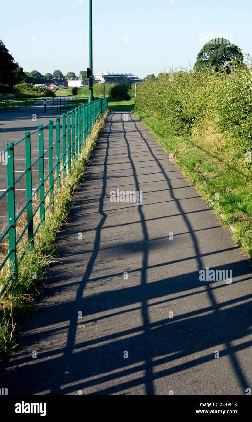 Fußweg mit Schatten von Geländern in der Nähe der Warwick Racecourse, Warwickshire, Großbritannien Stockfoto