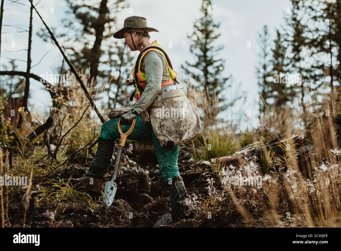 Waldarbeiter, der durch entwaldete Flächen im Wald geht und eine Tasche voller Bäume und eine Schaufel trägt. Frau, die in der Forstwirtschaft arbeitet. Stockfoto