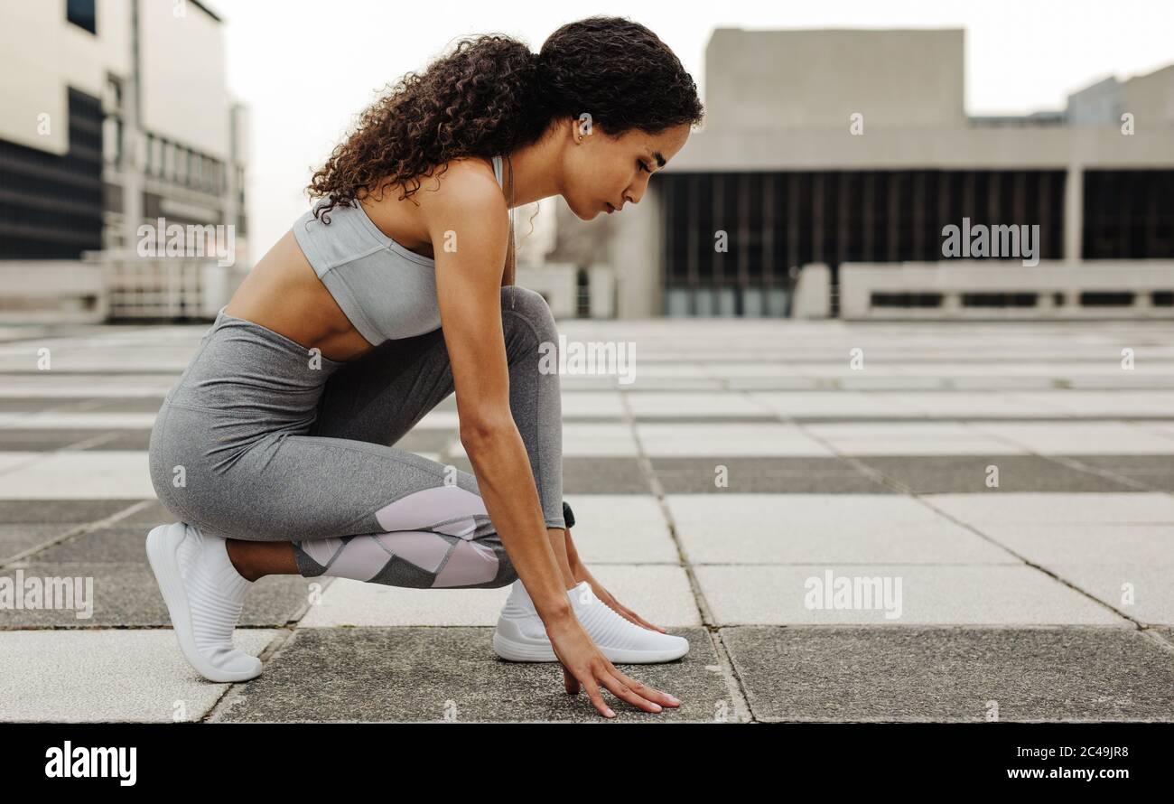 Seitenansicht einer Sprinterin in Startposition im Freien in der Stadt. Athletin in der Startposition. Stockfoto