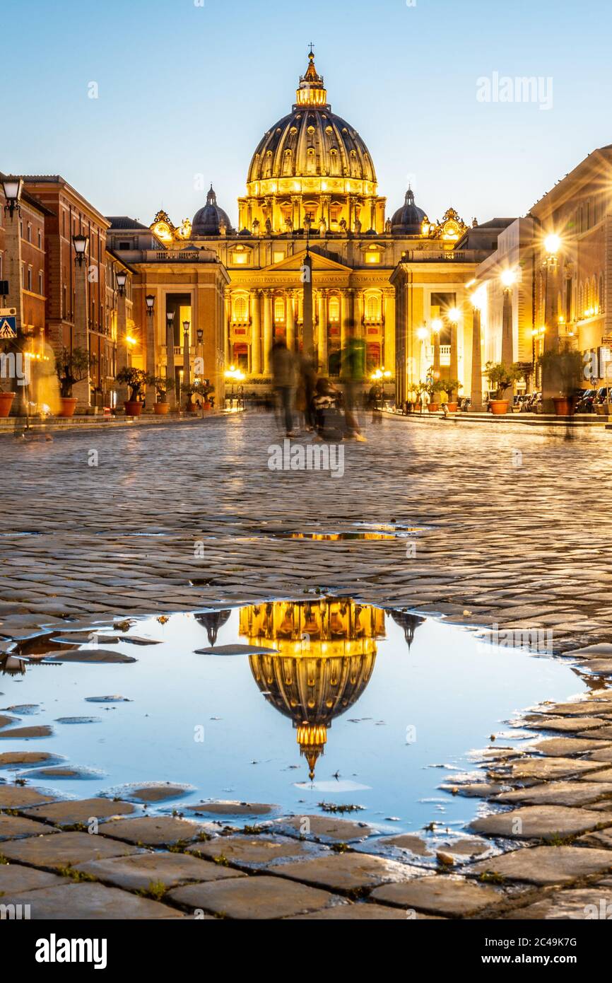 Vatikanstadt bei Nacht. Beleuchtete Kuppel der Petersbasilika und des Petersplatzes. Gruppe von Touristen auf der Via della Conciliazione. Rom, Italien. Stockfoto