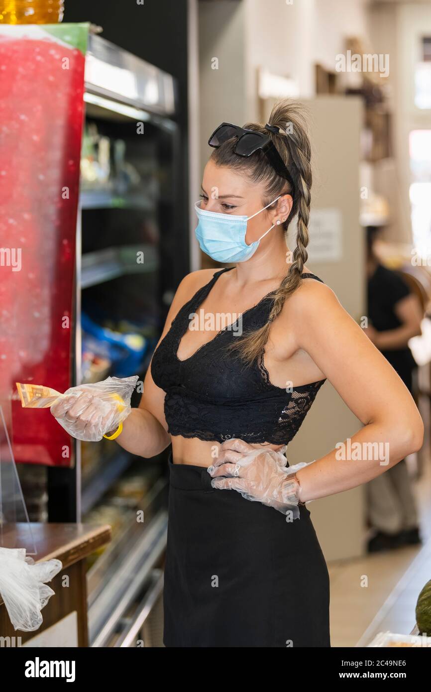 Frau trägt Sonnenbrille, eine OP-Maske und Plastikhandschuhe mit einer Euro- Rechnung auf ihrer rechten Hand auf einem unfokussierten Hintergrund.  Sicherheit und Einkaufen Stockfotografie - Alamy