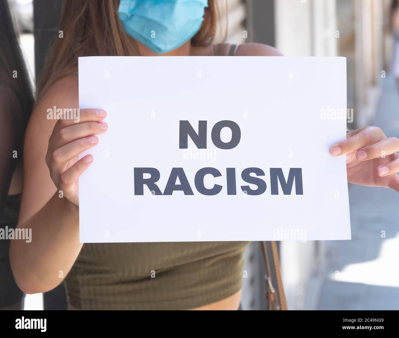 Nahaufnahme einer jungen Frau, die eine OP-Maske trägt und ein Schild mit einer Botschaft auf einem unfokussierten Hintergrund hält. Konzept für Sicherheit und Sensibilisierung. Stockfoto