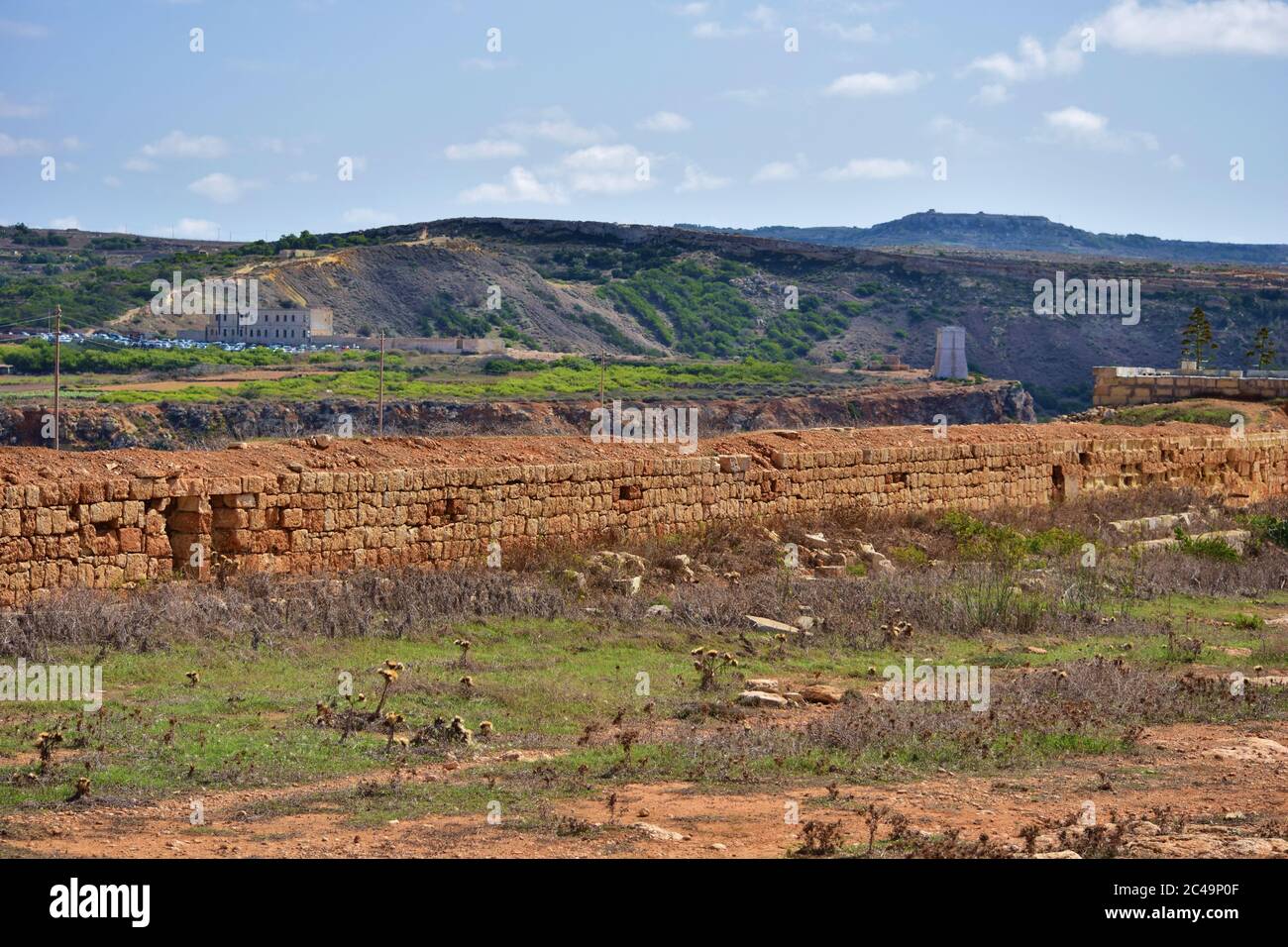 MELLIEHA, MALTA - 12. Okt 2014: Verteidigungsmauer aus Kalksteinblöcken in Ghajn Tuffieha, mit Ghajn Tuffieha Turm im Hintergrund, Malta Stockfoto