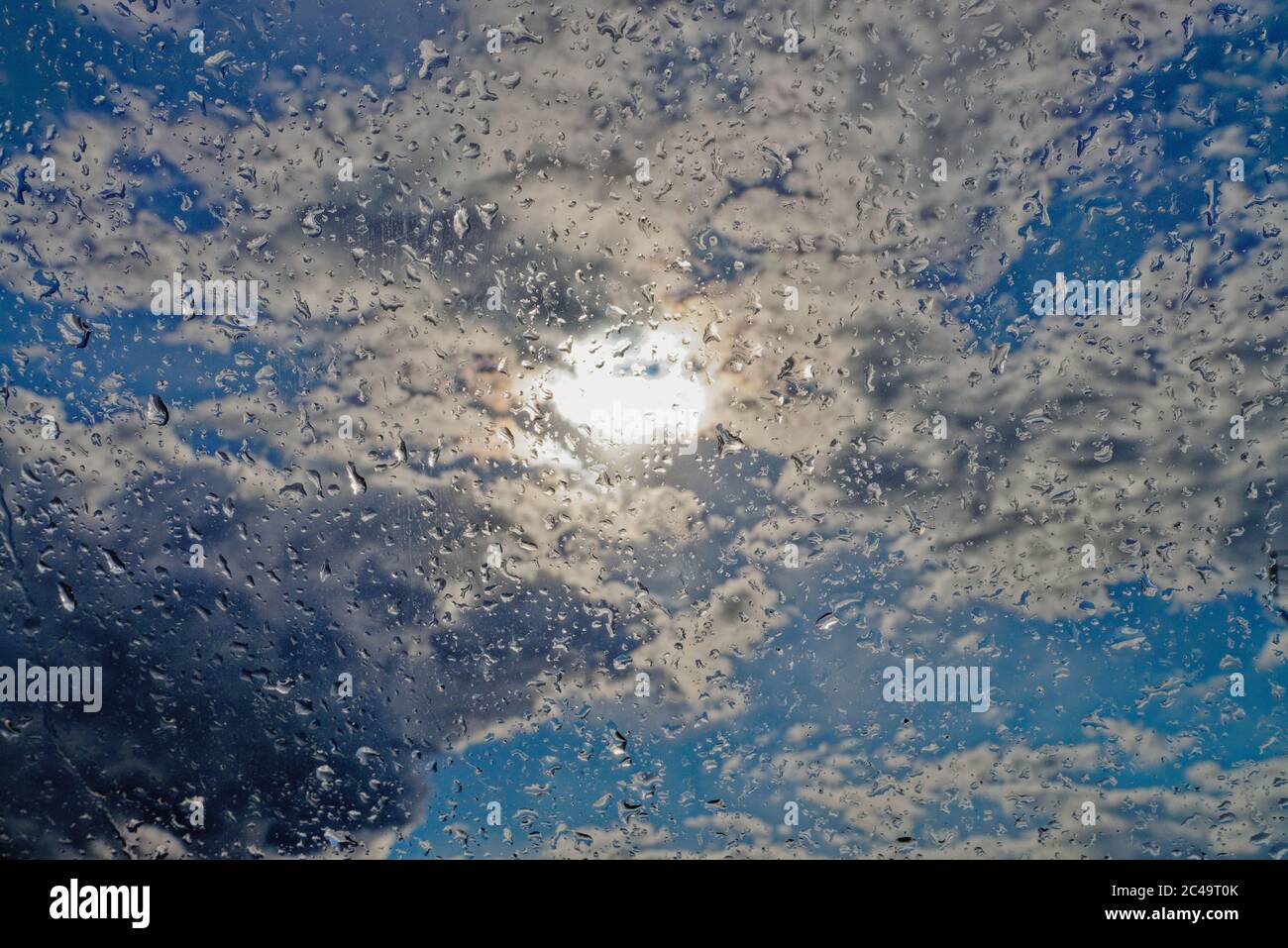 Nahaufnahme von Regentropfen auf einem Fenster vor dem Hintergrund der Sonne, Regenwolken und blauer Himmel Stockfoto