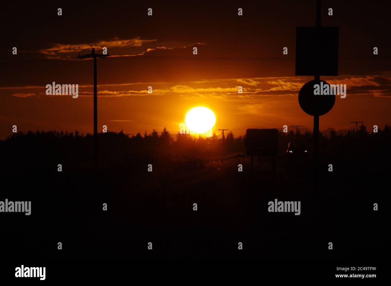 Bildfolge eines Sonnenuntergangs, untergehende Sonne am Ende der Straße, gelber Sonnenuntergang am Horizont über der Skyline von Kiefern, Island Silhouette im Vordergrund Stockfoto