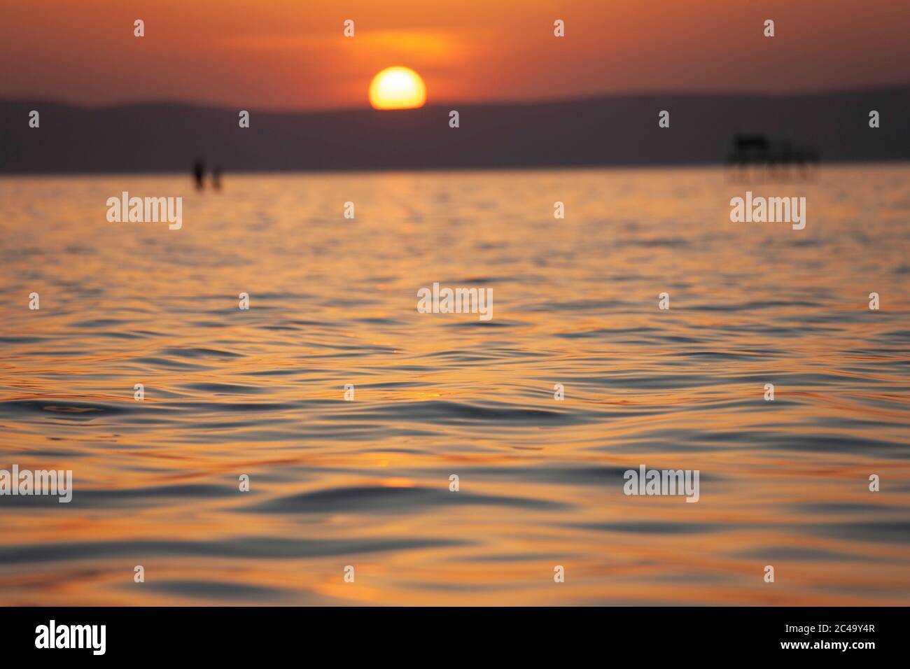 Verschwommener Sonnenuntergang über dem Plattensee in Ungarn. Fokussiert auf Wellen im Vordergrund Stockfoto