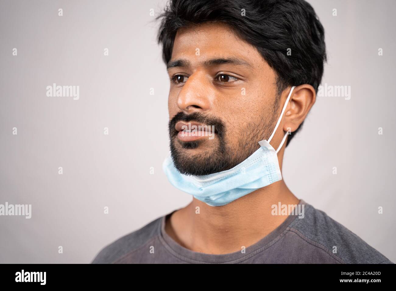 Konzept zeigt die unsachgemäße Art der Verwendung von Gesichtsmasken während Coronavirus oder covid-19 Krise - junger Mann trägt medizinische am Hals auf isoliertem Hintergrund Stockfoto