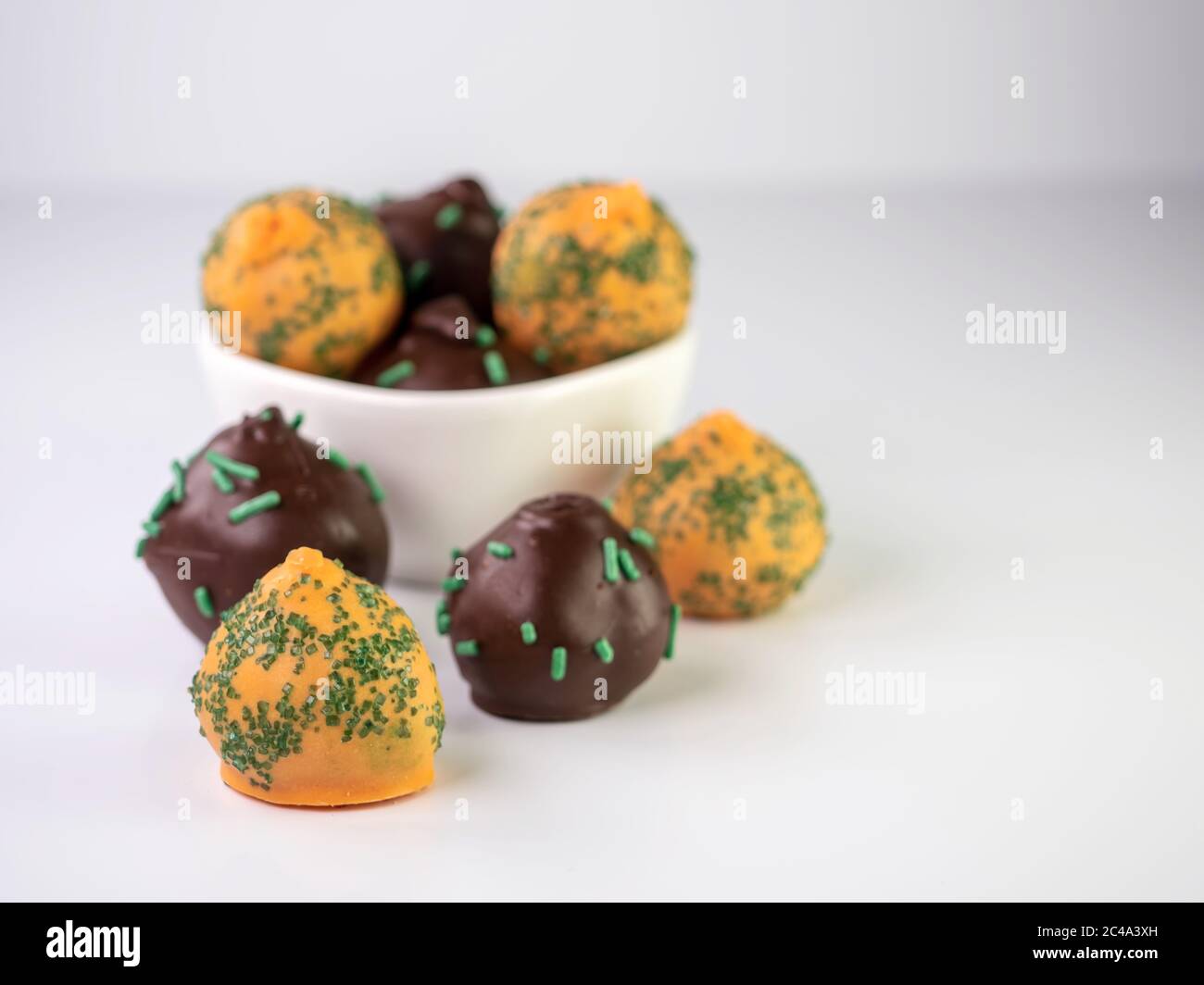 Karottenkuchenbällchen und Schokoladen-Minzkuchenbällchen mit Streuseln sitzen in einem weißen Braun und davor auf einer weißen Oberfläche. Stockfoto