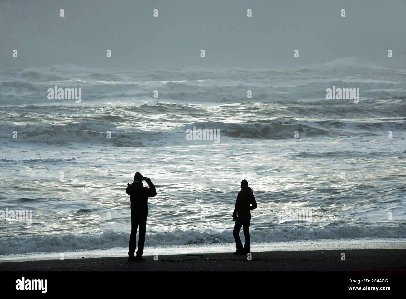 Zwei Silhouetten am Reynisfjara Beach, etwas westlich von Vik. Das Meer dahinter ist einige schöne silberne Meeresfarben. Stockfoto