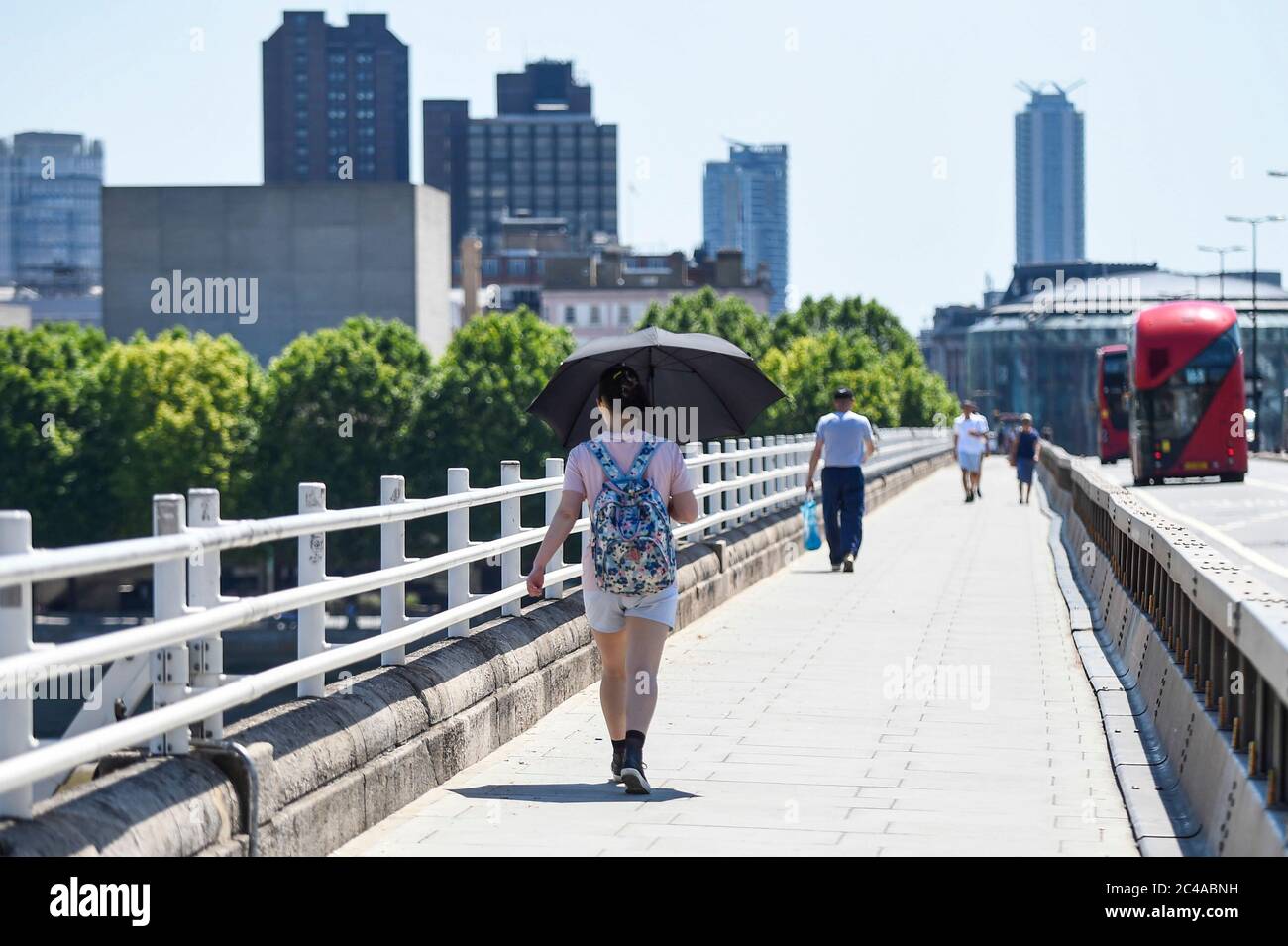 London, Großbritannien. 25. Juni 2020. UK Wetter: Eine Frau schützt sich vor der Hitze unter einem Regenschirm auf der Waterloo Bridge in der Sonne, an dem es den Prognosen zufolge der heißeste Tag des Jahres sein wird. Der UV-Index des MET Office wird aufgrund des klaren Himmels und der fehlenden Dampfspuren von Flugzeugen aufgrund der Reduzierung der Flüge während der Coronavirus-Pandemie voraussichtlich außergewöhnlich hoch sein. Kredit: Stephen Chung / Alamy Live Nachrichten Stockfoto