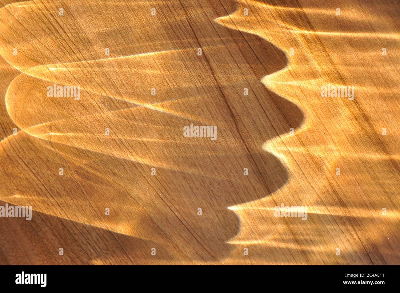 Abstraktes Muster, das durch Sonnenlicht entsteht, das durch eine Glasschale auf eine Holztischplatte strömt.Cornwall.UK Stockfoto