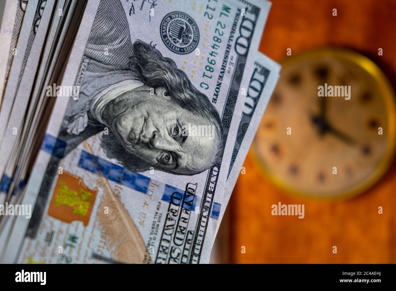 Nahaufnahme von vielen US-Dollar-Banknoten mit Vintage-Uhr auf dem Hintergrund. Zeit ist Geld-Konzept Stockfoto