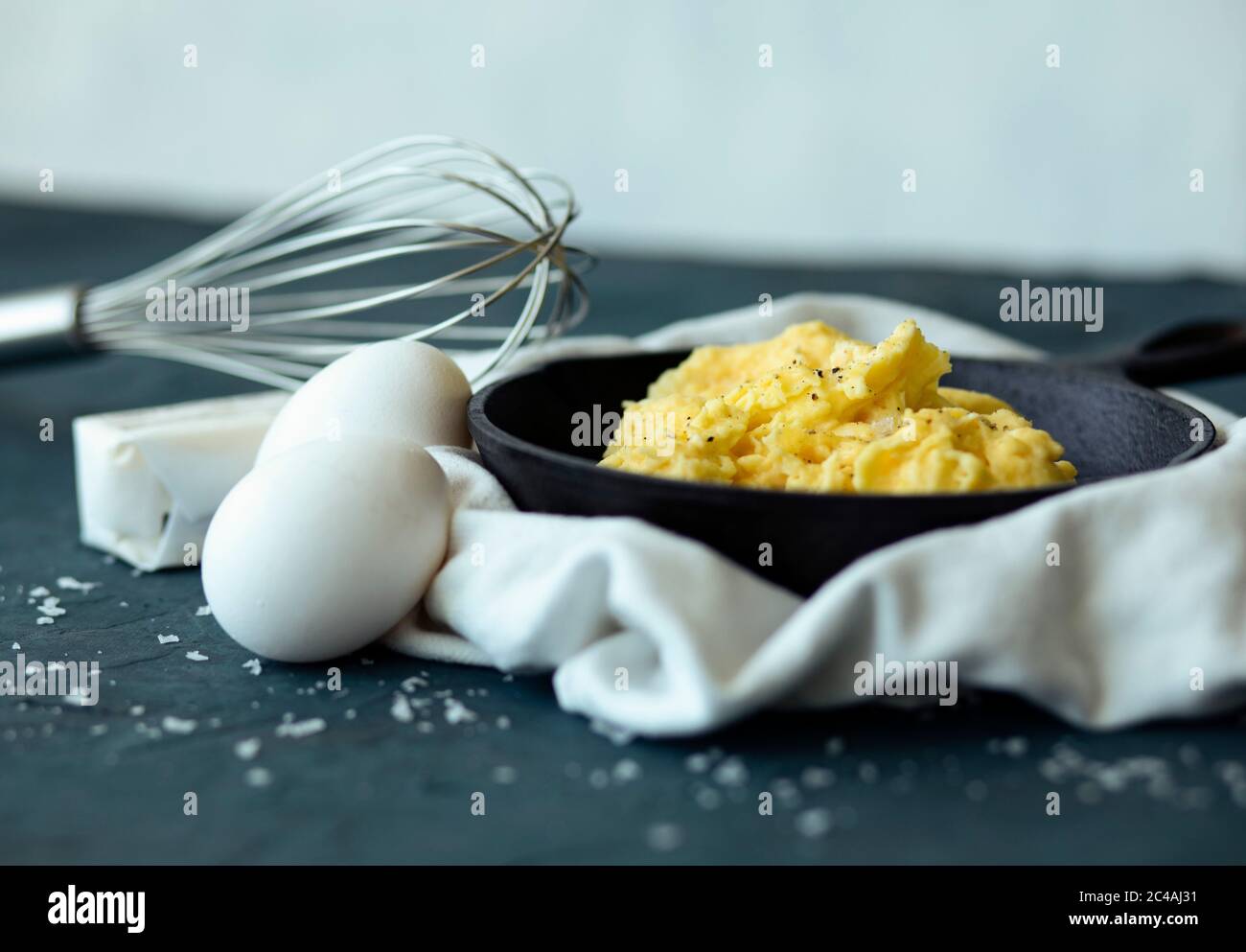 Köstliche Rühreier in gusseiserner Pfanne mit Schneebesen, Butter und Eiern Stockfoto