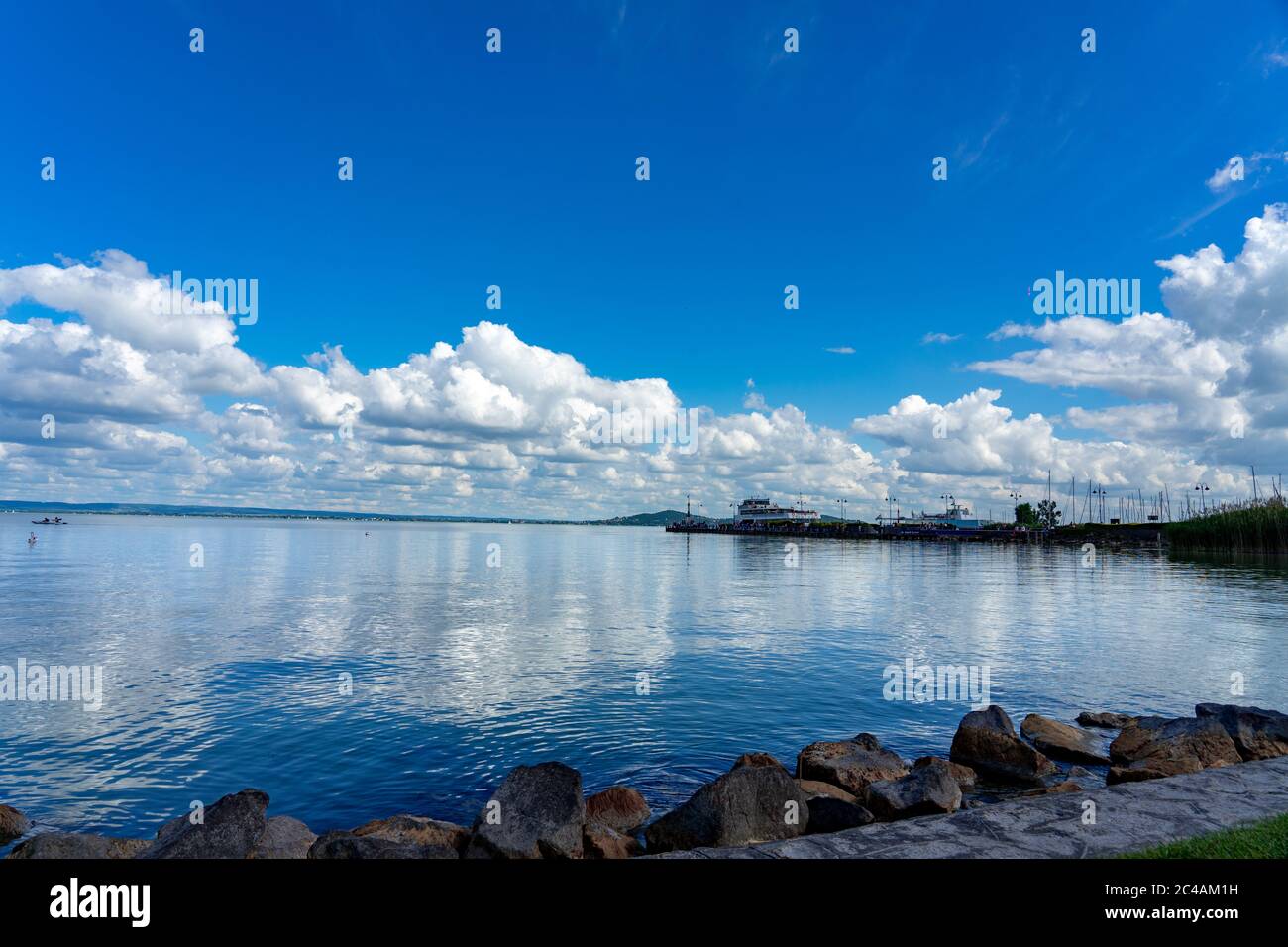 Badacsony Pier vom Strand am Plattensee in Ungarn mit blauem Himmel und Wolkenverfärbung auf dem Wasser. Stockfoto