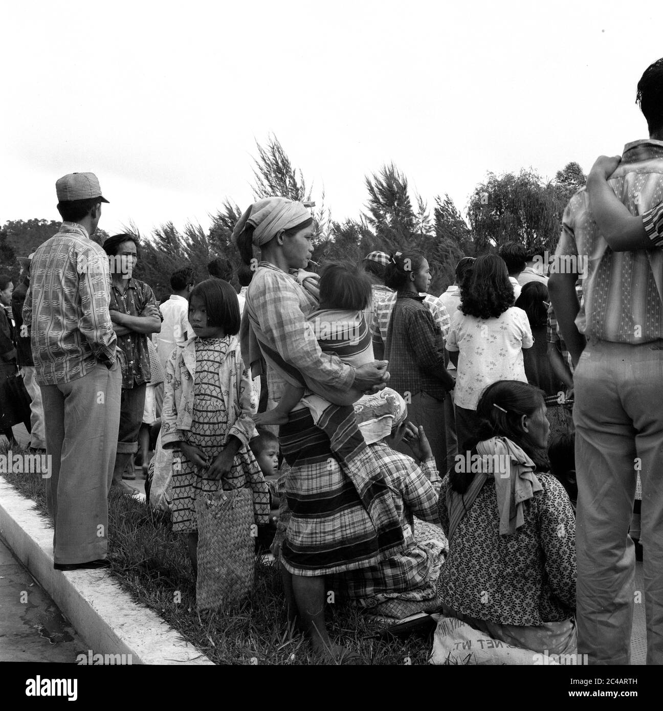 Menge von Menschen, die auf einen Bus warten 1959 Personen Straßenszene, Baguio City, Philippinen, mit Mutter, die einen Cheroot im Halter raucht, während sie ein Kind hält. Stockfoto