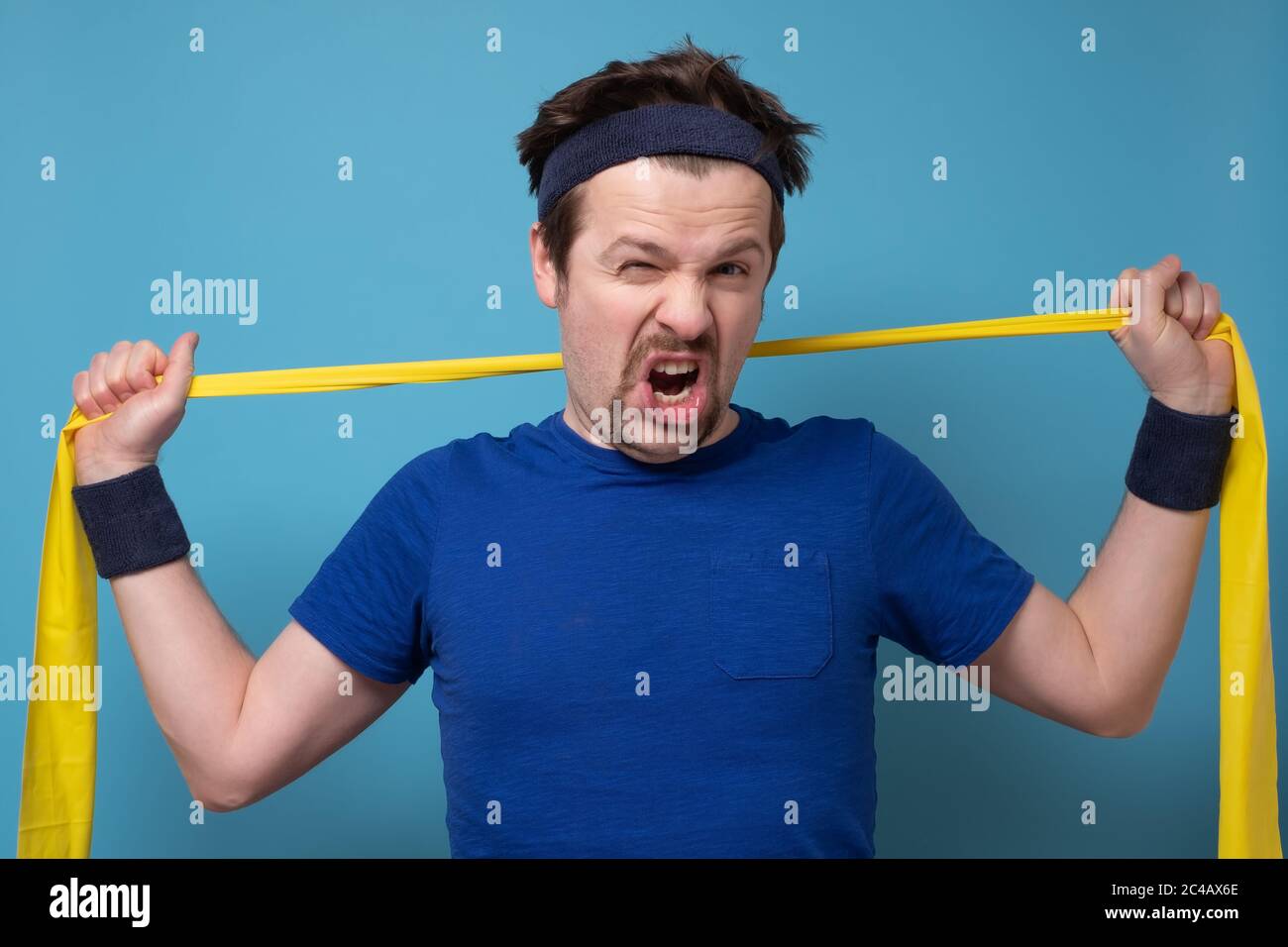 Athletischer Mann beim Training mit Gummiband an der blauen Wand. Stockfoto