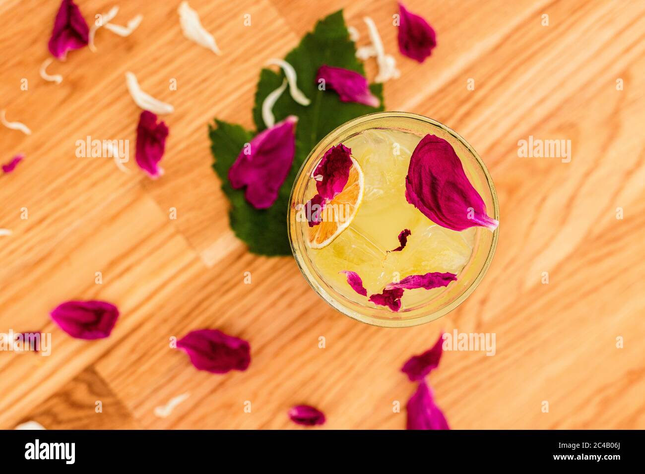 Ein erfrischender Zitruscocktail mit Eis in einem Steinglas, das mit einer trockenen Orangenscheibe und Rosenblättern dekoriert ist, von oben aus Stockfoto